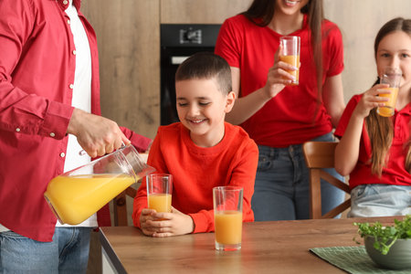 Father pouring orange juice in glass of his little son at homeの写真素材