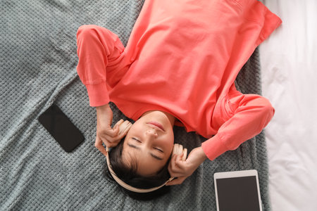 Little boy in headphones listening to music on bed, top viewの写真素材