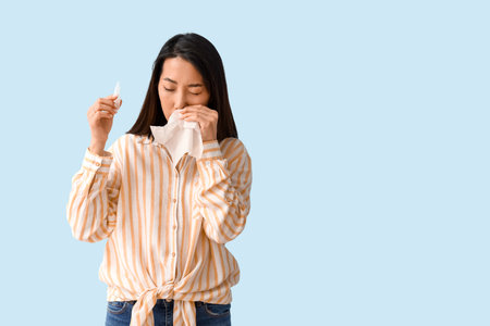 Allergic Asian woman with tissue and nasal drops on blue backgroundの写真素材