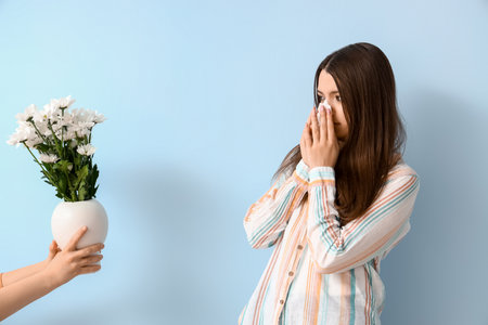 Allergic young woman and female hand with flowers on blue backgroundの写真素材