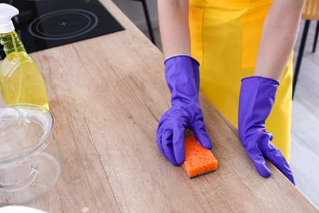 Woman in purple rubber gloves cleaning wooden countertop with spongeの写真素材