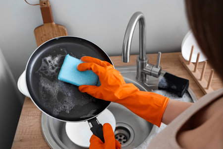 Woman in orange rubber gloves cleaning washing frying pan with spongeの写真素材