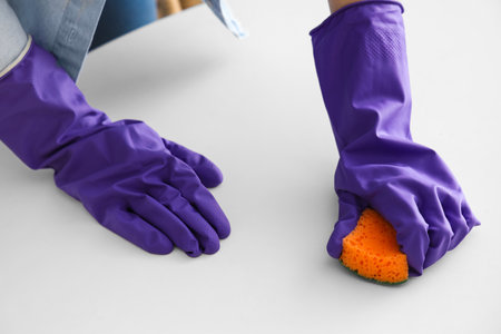 Woman in purple rubber gloves cleaning table with spongeの写真素材