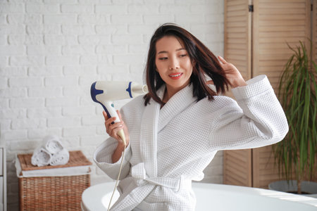 Pretty young Asian woman drying hair in bathroomの写真素材