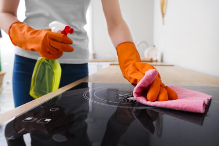 Woman in orange rubber gloves cleaning electric stove with rag and detergentの写真素材