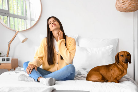Allergic young woman with dachshund dog scratching in bedroomの写真素材