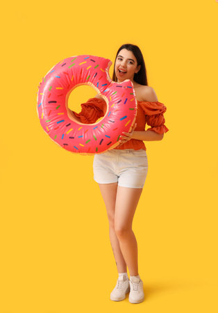 Young woman with inflatable ring in shape of donut on orange background