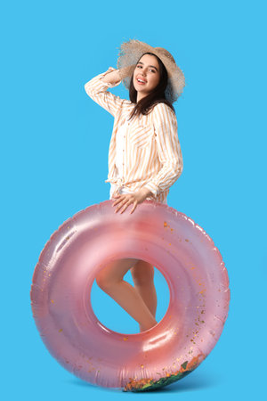 Young woman with pink inflatable ring on blue backgroundの写真素材