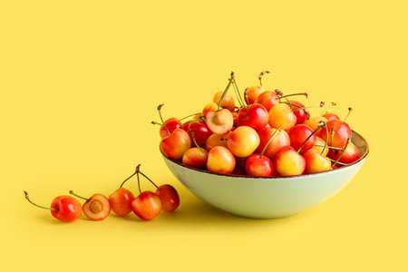 Bowl with sweet yellow cherry on color backgroundの写真素材