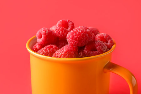 Cup with fresh raspberries on red backgroundの写真素材