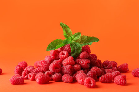 Heap of fresh raspberries and mint on orange background