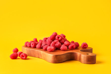 Wooden board with fresh raspberries on yellow backgroundの写真素材