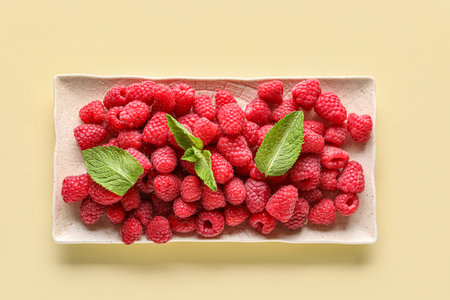 Plate with fresh raspberries and mint on yellow backgroundの写真素材