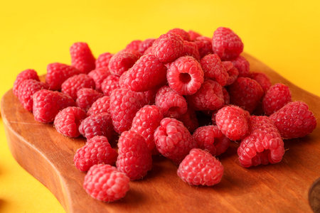 Wooden board with fresh raspberries on yellow background, closeup
