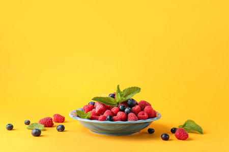 Plate with fresh raspberries and blueberries on yellow backgroundの写真素材