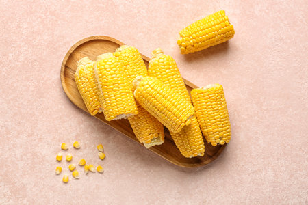 Wooden board with fresh corn cobs on pink backgroundの写真素材