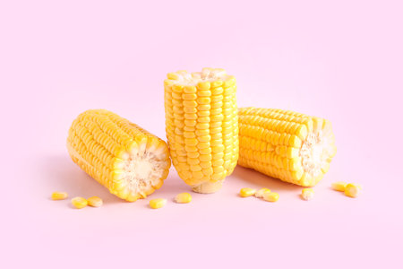 Cut fresh corn cobs and seeds on pink background