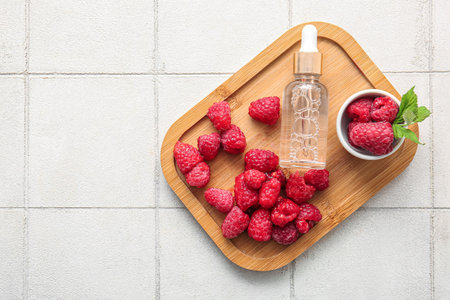 Wooden board with bottle of cosmetic raspberry oil on white tile backgroundの写真素材