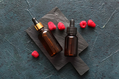 Board with bottles of cosmetic raspberry oil on dark backgroundの写真素材