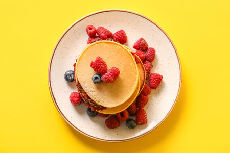Plate of tasty pancakes with raspberries and blueberries on yellow background