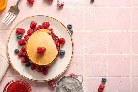 Plate of tasty pancakes with raspberries and blueberries on pink tile background