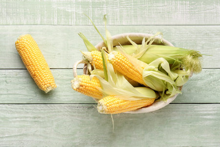 Wicker bowl with fresh corn cobs on green wooden backgroundの写真素材
