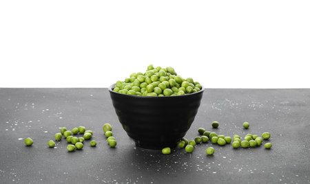 Bowl with fresh green peas on black table against white backgroundの写真素材