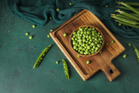 Bowl and wooden board with fresh green peas on color backgroundの写真素材