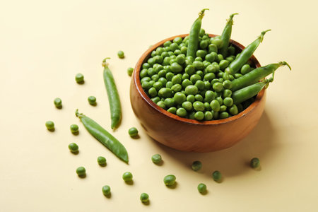 Bowl with fresh green peas on yellow background