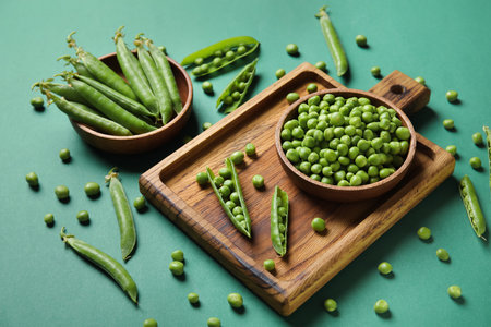 Bowls and wooden board with fresh green peas on color backgroundの写真素材