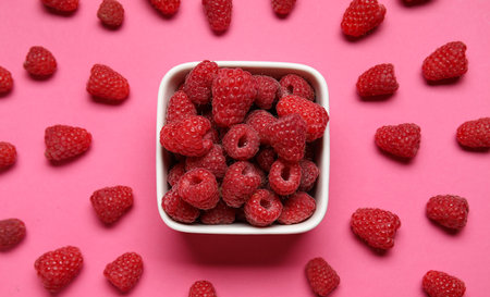 Bowl with fresh raspberries on pink background