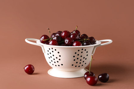 Colander with sweet cherry on brown background