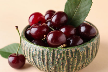 Bowl with sweet cherry and leaves on beige background