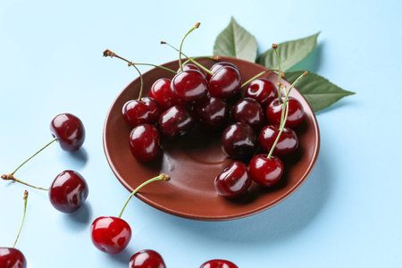 Plate with sweet cherry and leaves on blue background