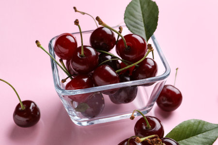Glass bowl with sweet cherry and leaves on pink backgroundの写真素材