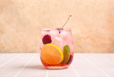 Glass of tasty cherry lemonade with lime and mint on pink tile table