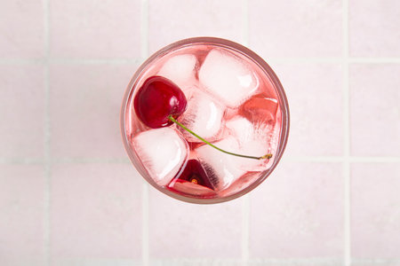 Glass of tasty cherry lemonade on pink tile backgroundの写真素材
