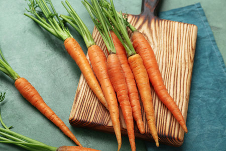 Fresh carrots and wooden board on green textured backgroundの写真素材