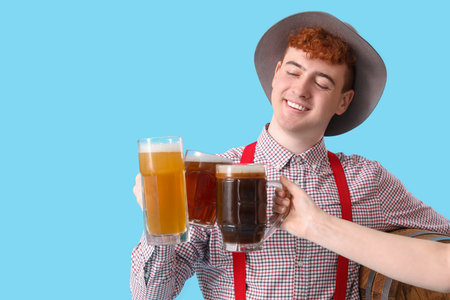Young man in traditional German clothes with beer clinking on blue background