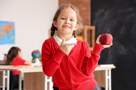 Little school girl with apple in classroom