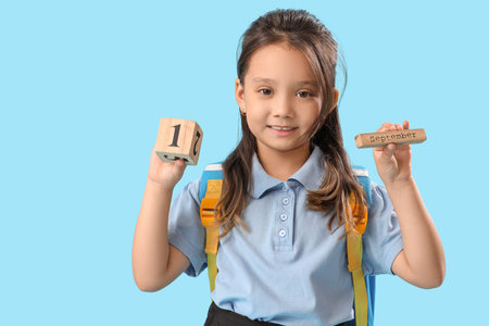Little school girl with calendar on light blue background