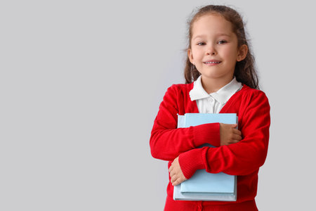 Little school girl with books on gray backgroundの写真素材