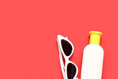 Sunglasses with bottle of sunscreen cream on red backgroundの写真素材
