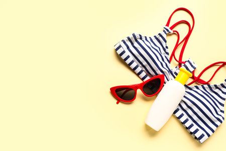 Sunglasses with bikini bra and bottle of sunscreen cream on pale yellow backgroundの写真素材