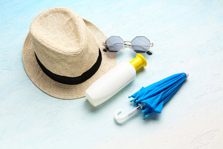 Wicker hat with sunglasses, mini umbrella and bottle of sunscreen cream on gradient background