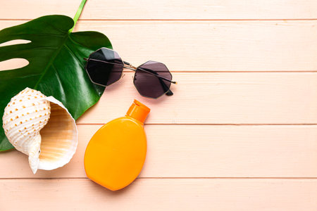 Sunglasses with palm leaf, seashell and bottle of sunscreen cream on pink wooden backgroundの写真素材