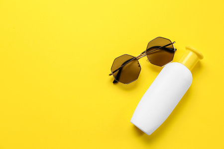 Sunglasses with bottle of sunscreen cream on yellow background