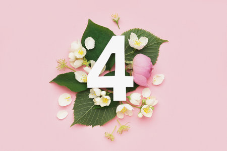 Green leaves and flowers with paper number four on pink background