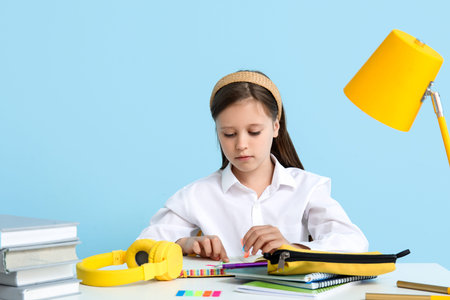 Little girl doing lessons at table on blue background