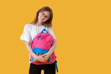 Female student with backpack on yellow background